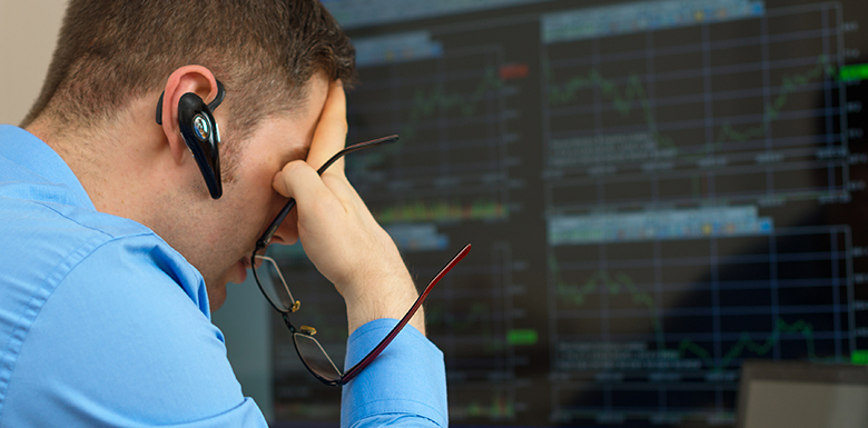 Stock broker looking at computer screen with his head in one of his hands