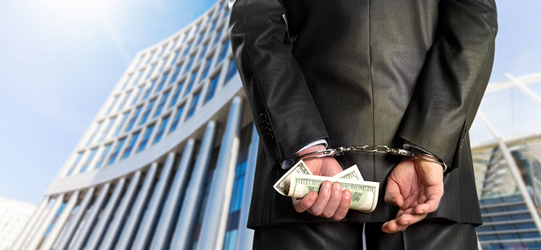 Man in suit wearing handcuffs holding hundred dollar bills