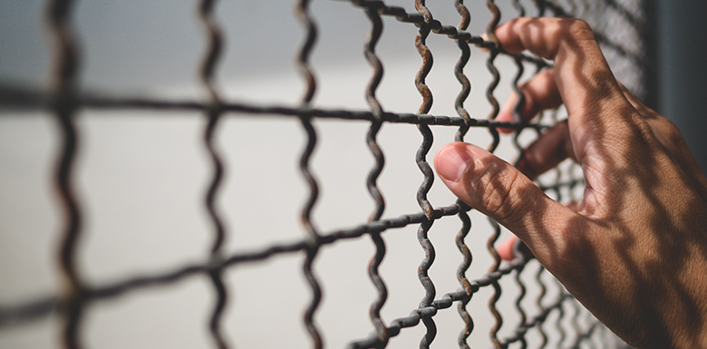 Hand clinging to prison bars